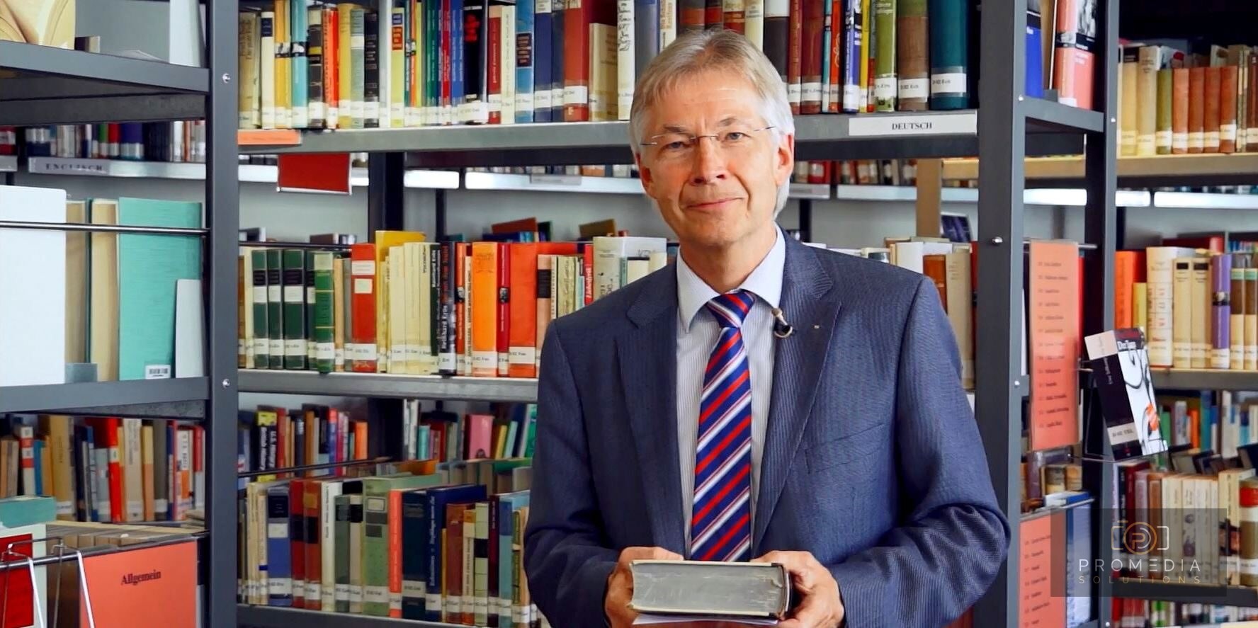 Mann im Anzug mit Buch vor einem Bücherregal