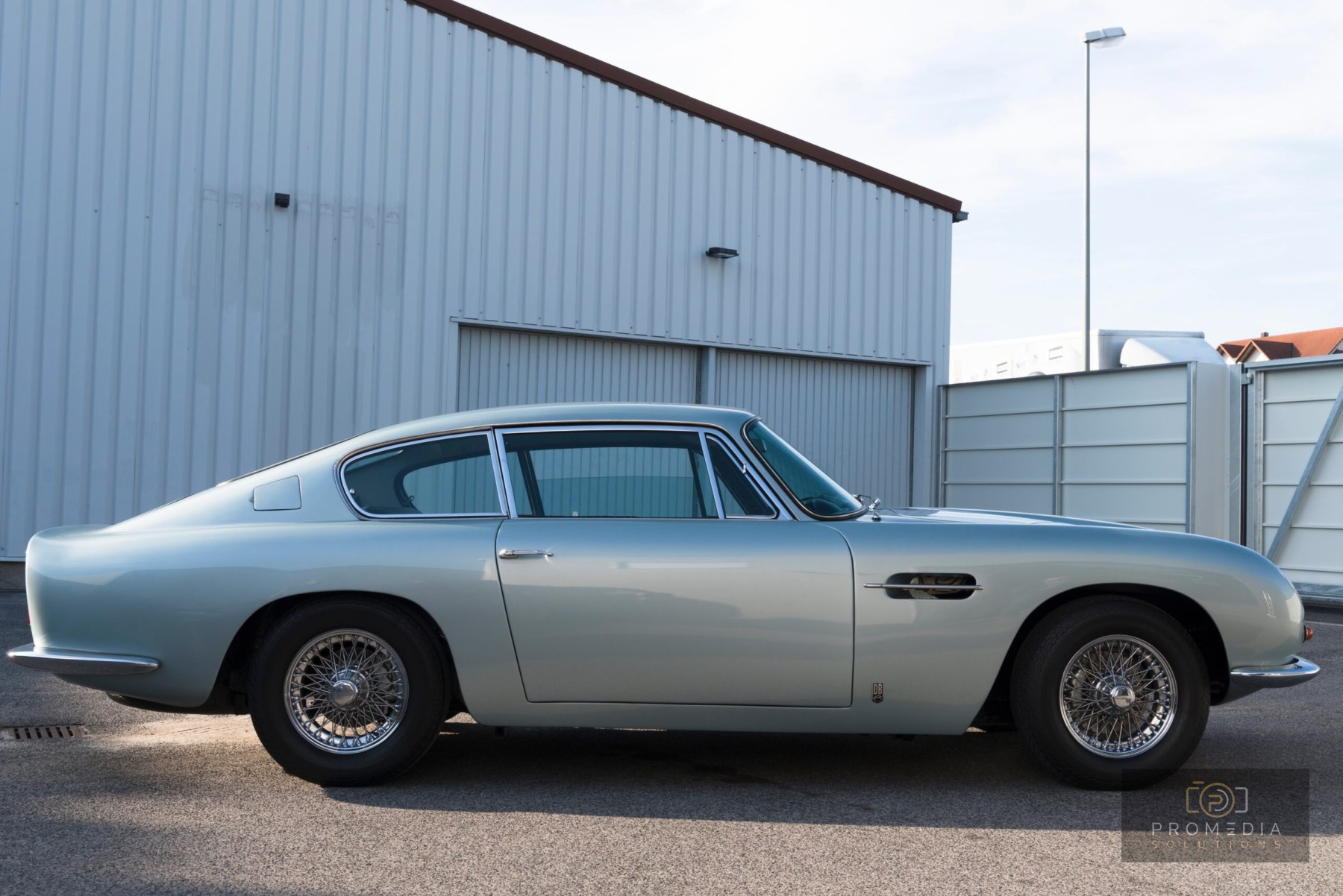 Silberner Aston Martin DB6 in der Seitenansicht vor einer Werkhalle